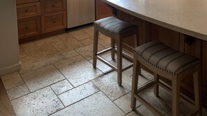 A kitchen with a large window, wooden cabinets, a sink, and a bar stool.