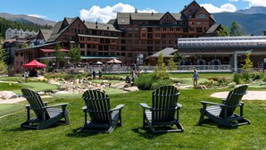 Una cabaña con un edificio grande, zona de estar al aire libre con sillas Adirondack y un campo de golf.