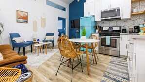 Una cucina moderna con mobili bianchi, un frigorifero blu ed elettrodomestici in acciaio inossidabile. C'è una zona pranzo con sedie in vimini e un tavolo bianco.