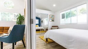 Una camera da letto moderna con un letto grande, una poltrona blu, un divano marrone e un'ampia finestra con persiane.