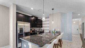 A modern kitchen with a granite countertop, stainless steel appliances, and white bar stools.
