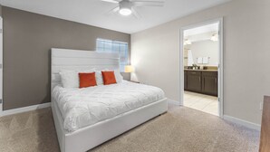A bedroom with a large bed, a ceiling fan, and a view into the kitchen.
