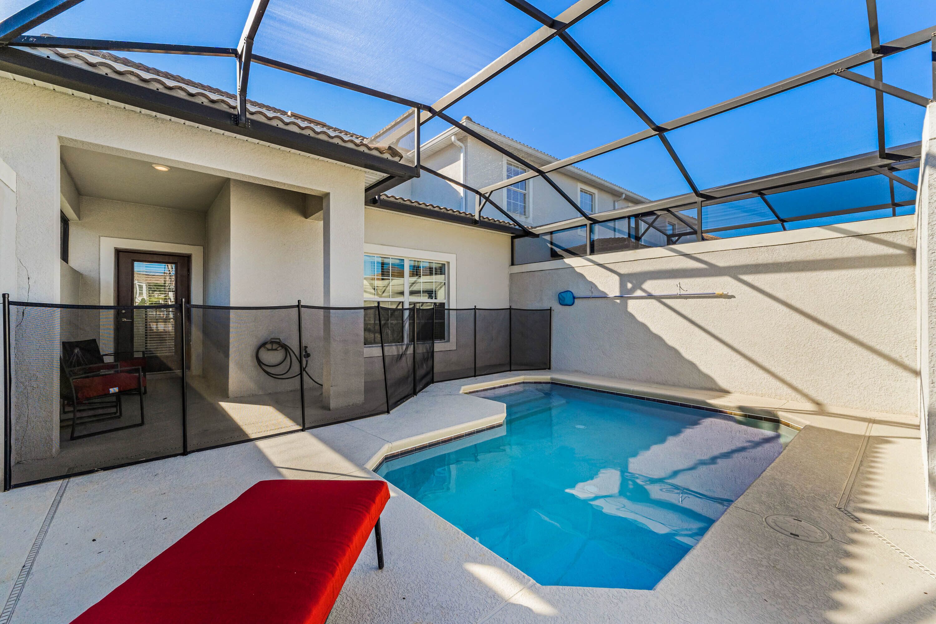 A swimming pool with a glass enclosure, a red bench, and a door leading to an interior space.