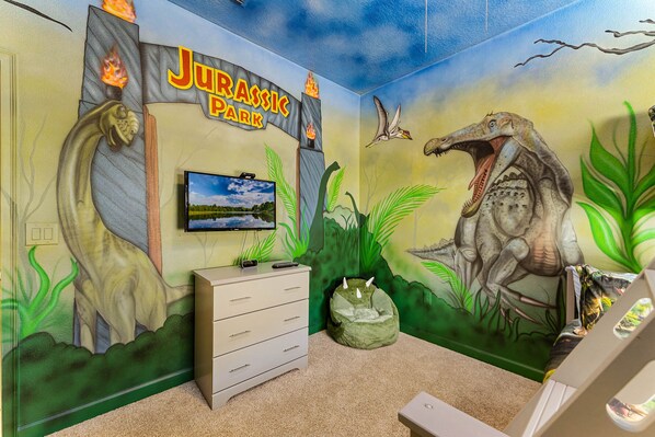 A room with a mural of a dinosaur, a sign reading "Jurassic Park", and a television on the wall.
