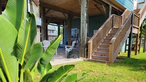 Un espace extérieur abrité, doté d’un escalier en bois, d’une pelouse et de grandes plantes vertes.