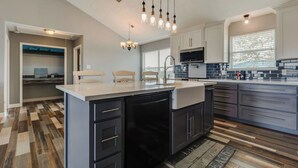 Une cuisine moderne dotée d’un îlot central, de meubles de rangement aux couleurs sombres et d’un parquet en bois disposé en motif chevrons.