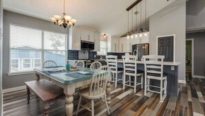Une cuisine moderne avec des meubles blancs, un grand îlot central et un coin repas comprenant une table et des chaises en bois.
