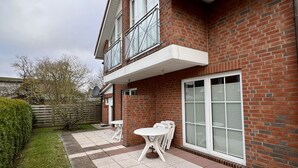 A two-story brick house with a balcony, a patio with a table and chairs, and a well-maintained lawn.