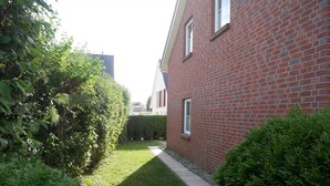 A narrow pathway leading to a red brick building with a small window.