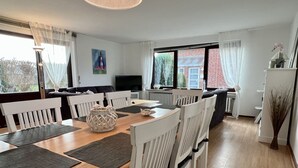 Un comedor moderno con una mesa de madera, sillas blancas y un televisor al fondo.