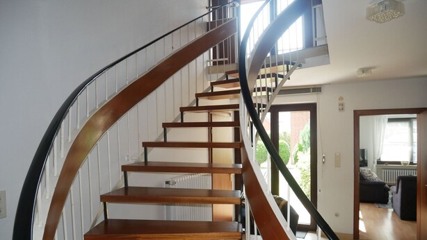 Una escalera de caracol con peldaños de madera y barandillas de metal, que conduce a un piso superior.