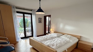 Un dormitorio con una cama de madera, una silla, una mesita de noche, una lámpara y vistas al exterior a través de una puerta de cristal.