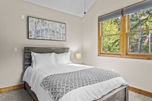 A bedroom with a bed, a window with a view of trees, and a painting on the wall.