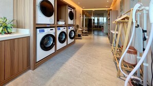 Un cuarto de lavado con varias lavadoras, armarios de madera y una zona de estar con sillas y una mesa.