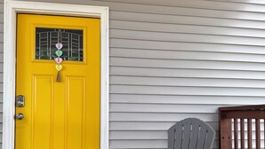 A yellow door with a window, a gray Adirondack chair, and a wooden fence.