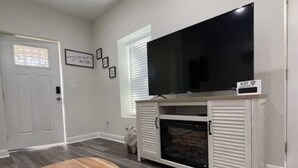 A living room with a large flat-screen TV, a white entertainment unit, and a grey patterned rug.