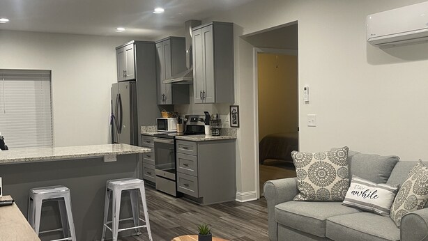A modern kitchen with grey cabinets, a central island, and a dining area with a grey sofa and patterned cushions.