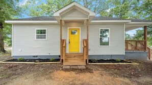 A single-story house with a yellow front door, a small porch, and a fenced backyard.