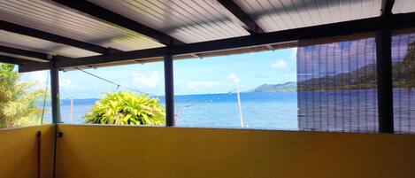 A room with a yellow wall, a tiled floor, and a view of the sea through large windows.