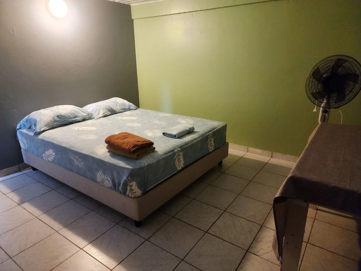A bedroom with a bed, a bedside table, and a standing fan.