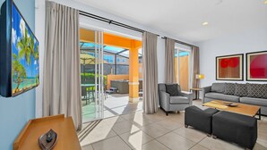 A modern hotel room with a large sliding glass door leading to an outdoor area, a sofa, a coffee table, and a TV on the wall.