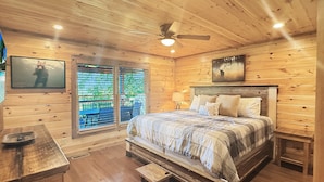 Camera da letto in una baita di legno, con un letto, una ventola a soffitto e una finestra vista verde.