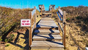 En træpromenade der fører hen til liggestole, med et skilt der står 'KEEP OFF THE DUNES'.
