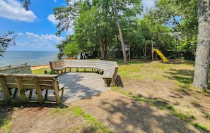 A wooden deck with benches, a playground with a slide, and a view of the sea.