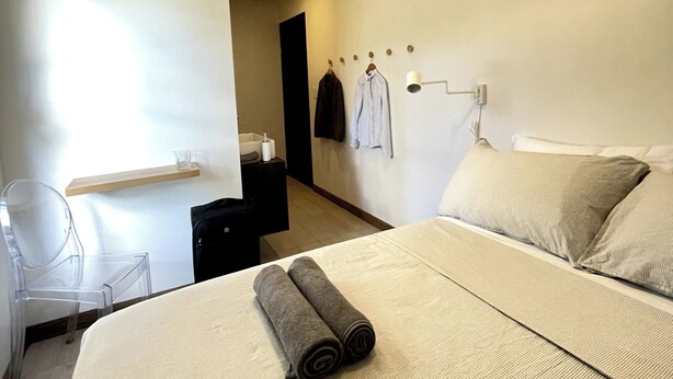 Une chambre d’hôtel moderne dotée d’un grand lit, d’un bureau avec une chaise, d’un porte-serviettes et d’une petite étagère contenant des articles de toilette.