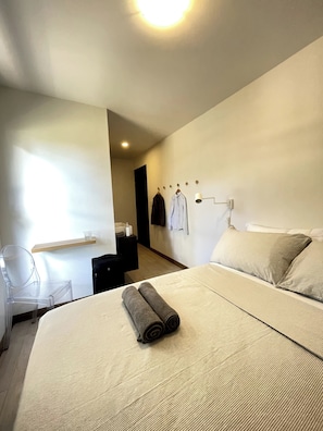 Een moderne hotelkamer met een groot bed, een bureau met stoel, een wandrek voor handdoeken en een klein plankje met toiletartikelen.