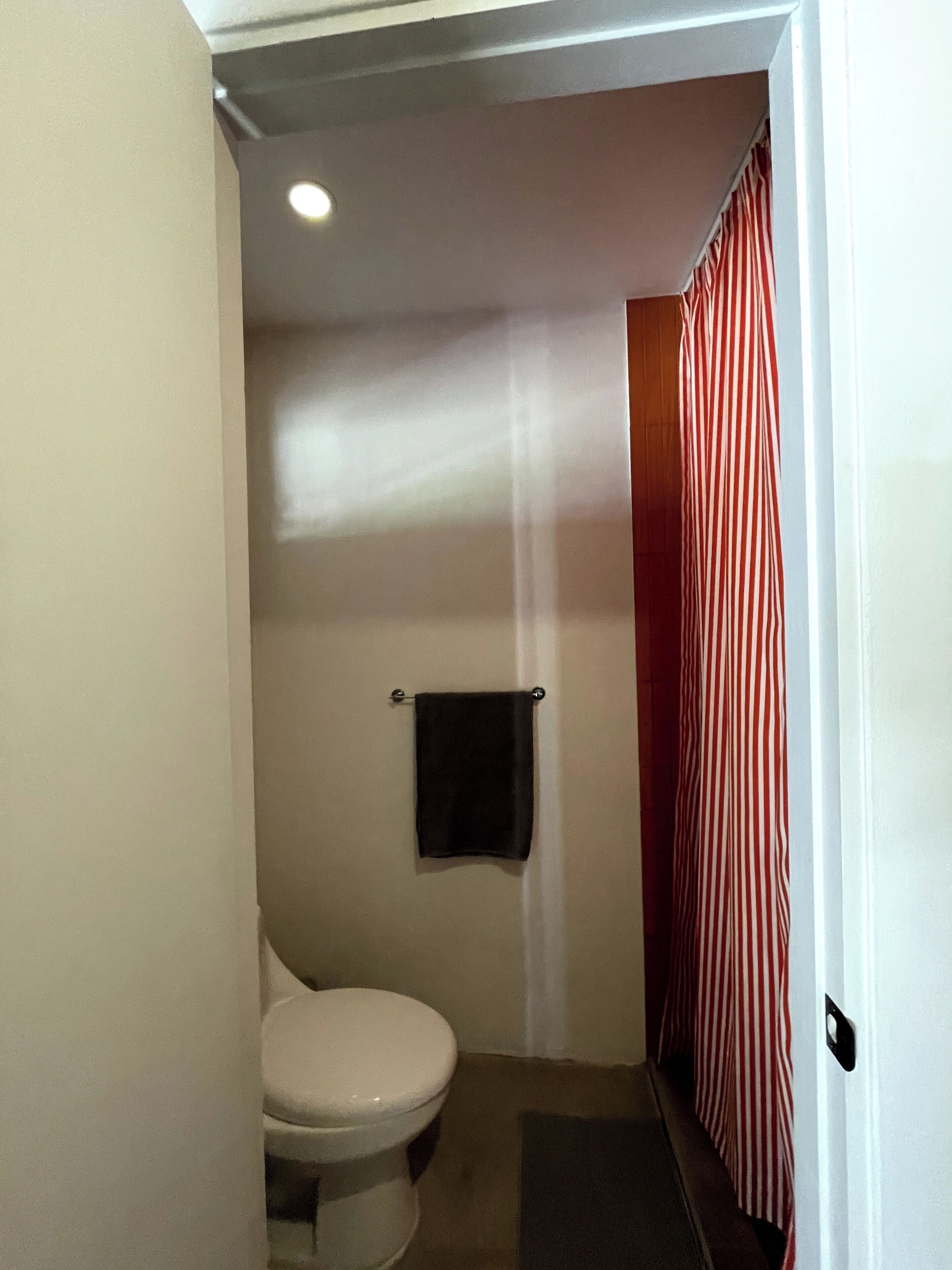 A small, narrow bathroom with a toilet, a towel hanging on the wall, and a striped curtain.