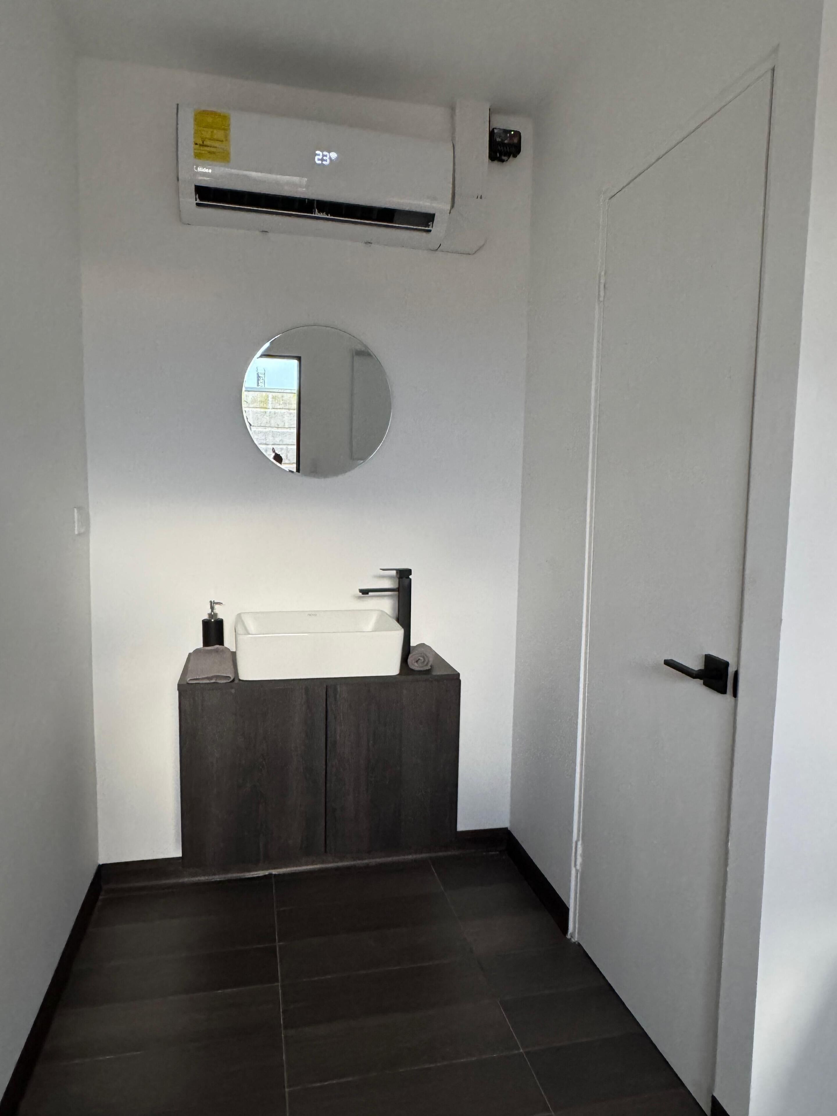 Une salle de bain avec un lavabo blanc, un meuble-lavabo en bois foncé, un miroir rond et une porte blanche.