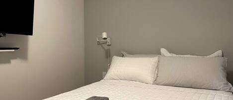 A neatly made bed with white and striped pillows, a rolled-up gray towel, and a white wall-mounted TV.