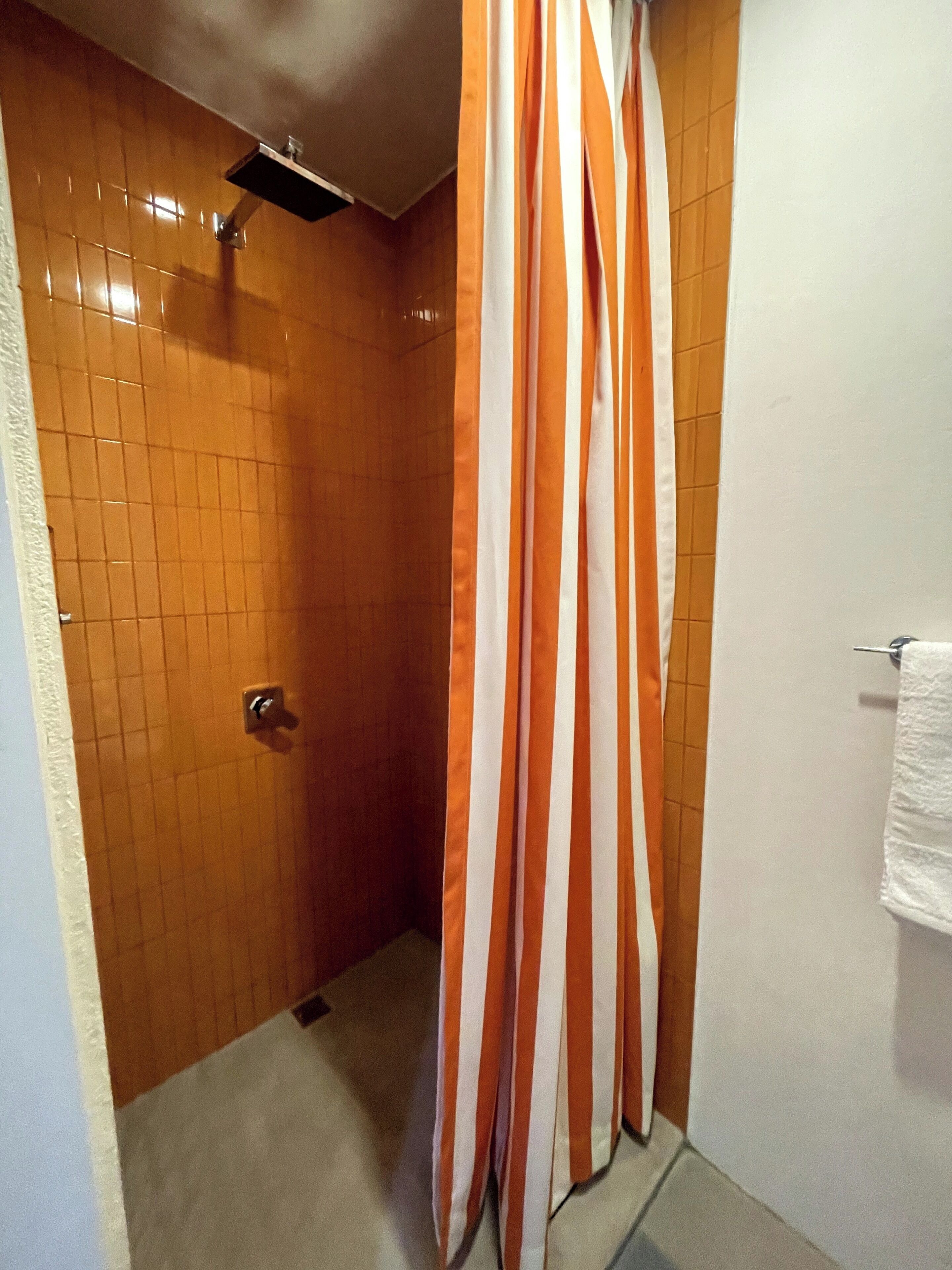 Een badkamer met oranje betegelde wanden, een douchegordijn en een handdoekrek.