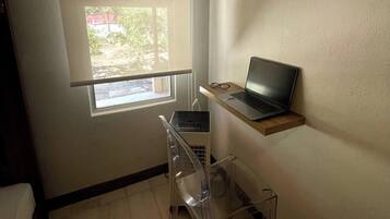 Een kleine kamer met een raam, een laptop op een plank en een transparante stoel.