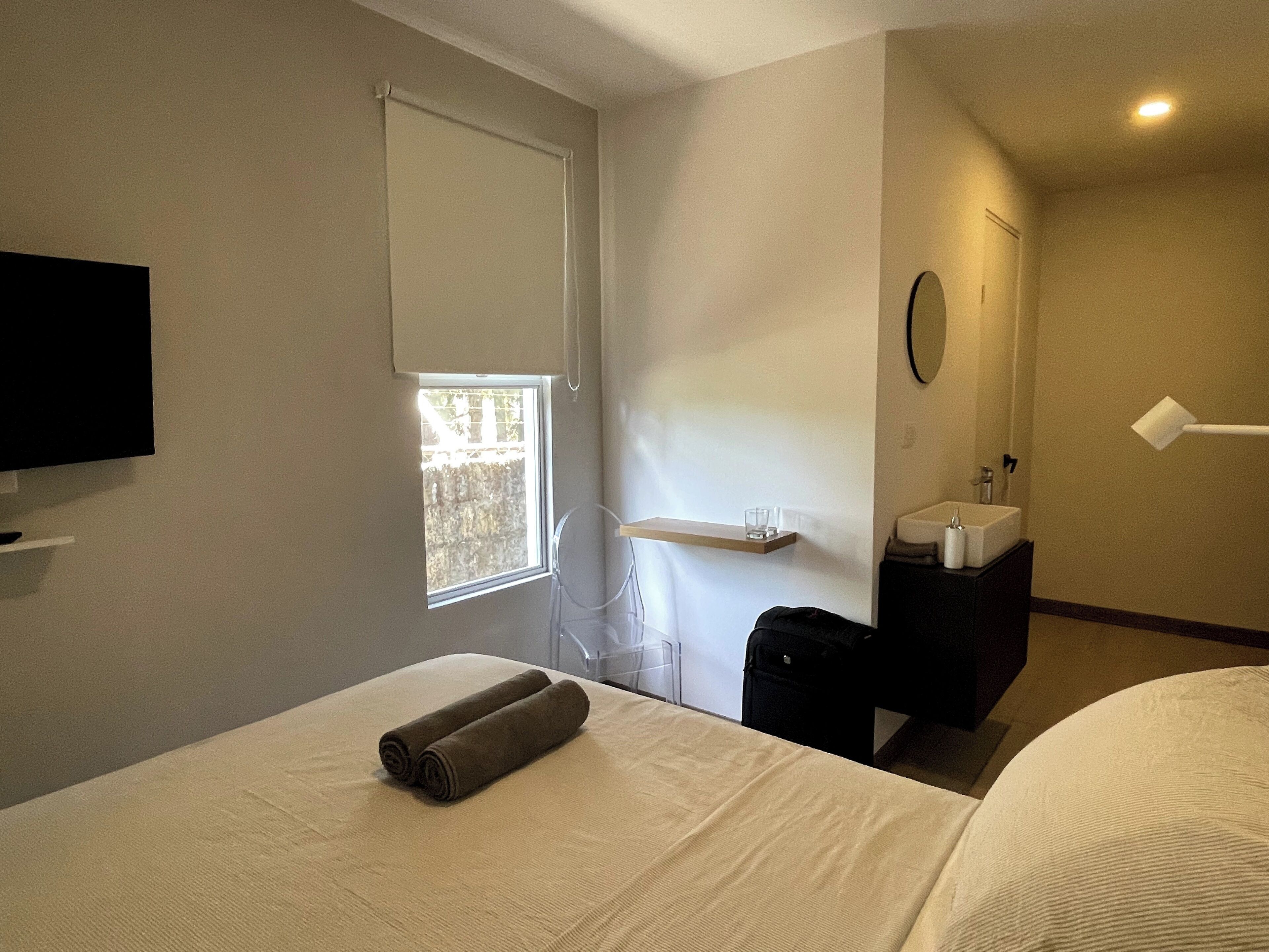 A hotel room with a bed, a TV, a window, a sink, and a mirror.