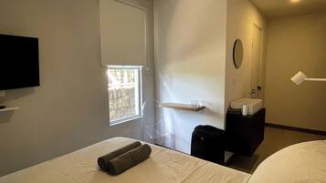 A hotel room with a bed, a TV, a window, a sink, and a mirror.
