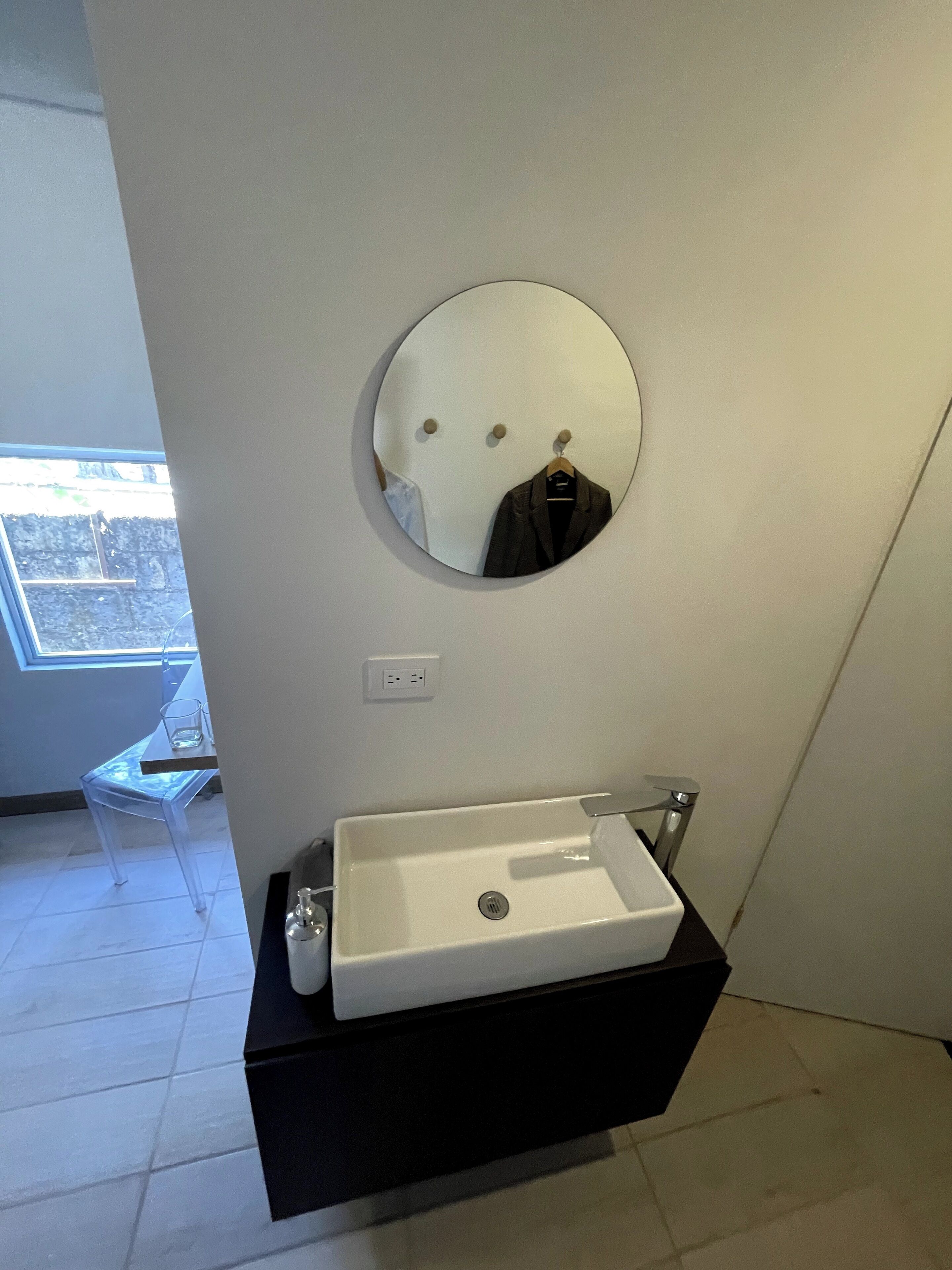 A bathroom with a white sink, a round mirror, and a black vanity.