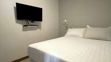 A bedroom with a bed, a flat-screen TV mounted on the wall, and a white wall.