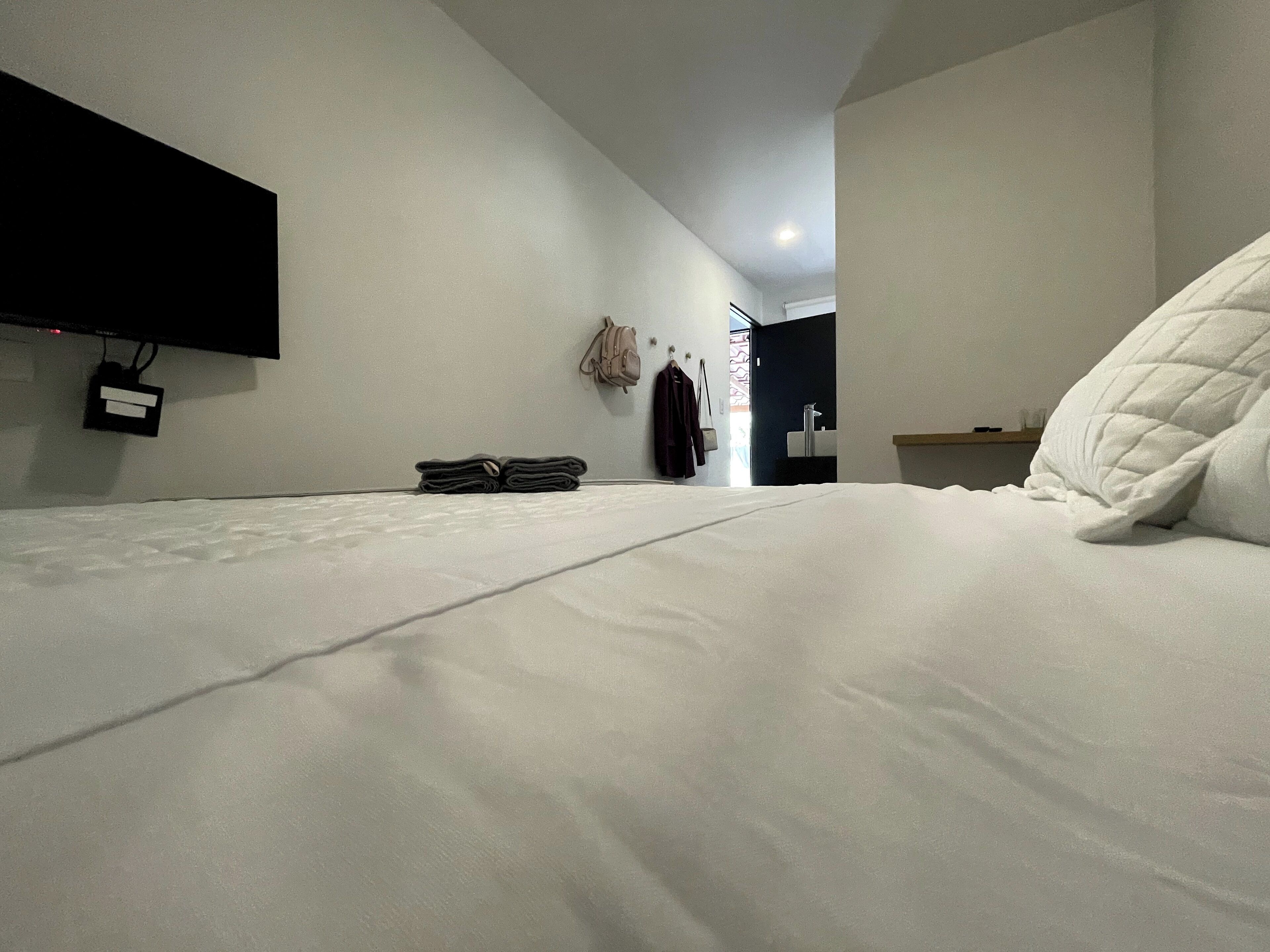 Una habitación de hotel moderna con una cama bien tendida, un televisor de pantalla plana en la pared y una mesita de noche con una lámpara.