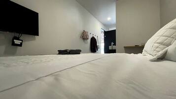Una habitación de hotel moderna con una cama bien tendida, un televisor de pantalla plana en la pared y una mesita de noche con una lámpara.