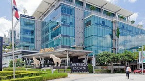 Un bâtiment moderne aux façades vitrées, une entrée imposante surmontée d’un auvent et une enseigne indiquant « AVENIDA ESCAZU ».