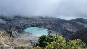 Un cratère volcanique abritant un lac aux eaux turquoise, entouré d’un paysage accidenté et d’une végétation clairsemée.