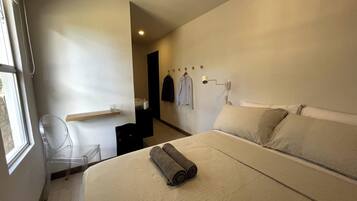 Una habitación de hotel con una cama, una silla, una mesita y una lámpara en la pared.
