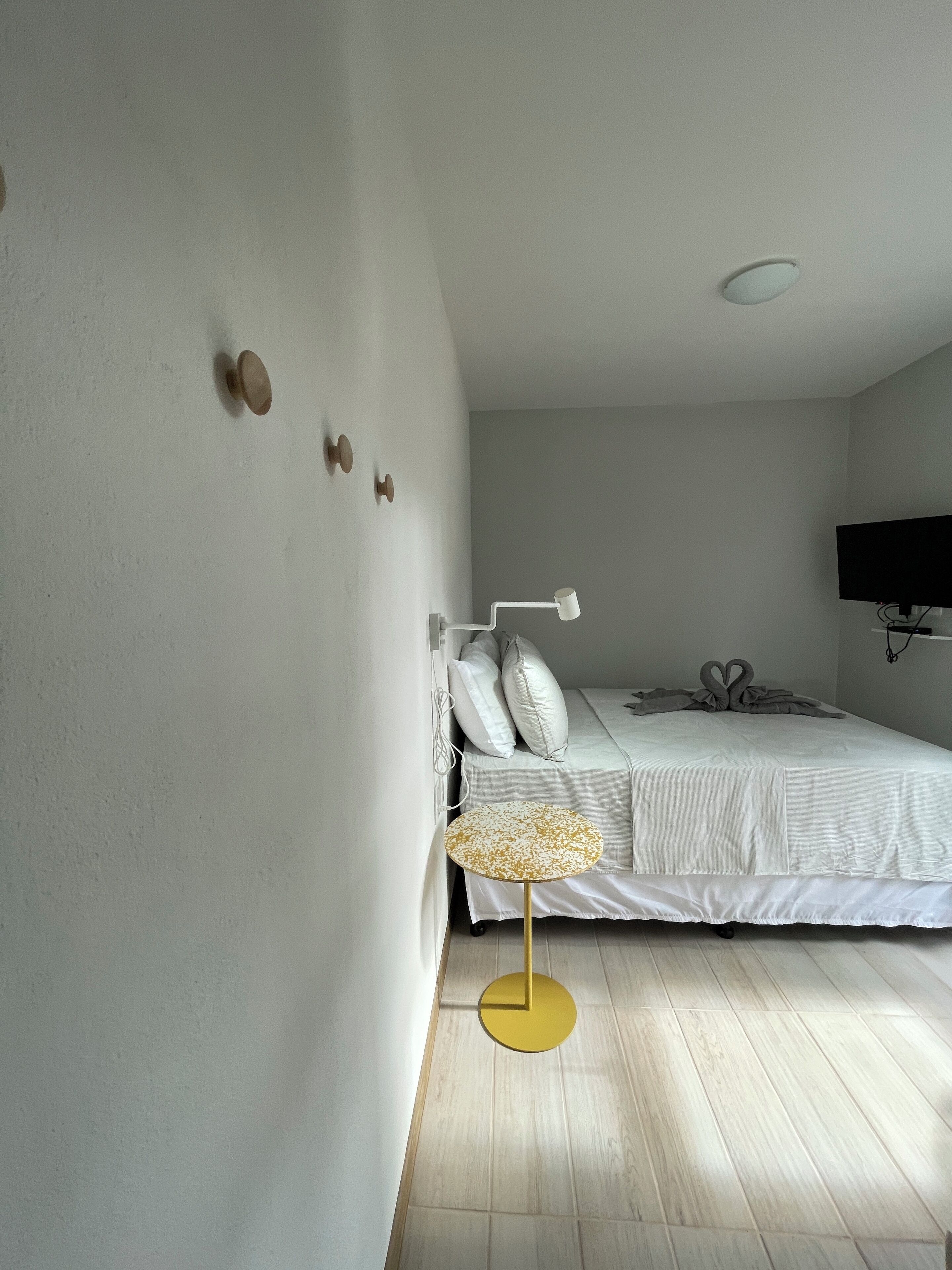 A bedroom with a bed, a bedside table, a lamp, a TV, and a wall-mounted light fixture.
