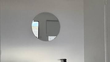 A bathroom with a white sink, dark wooden vanity, a round mirror, and an air conditioning unit above the mirror.