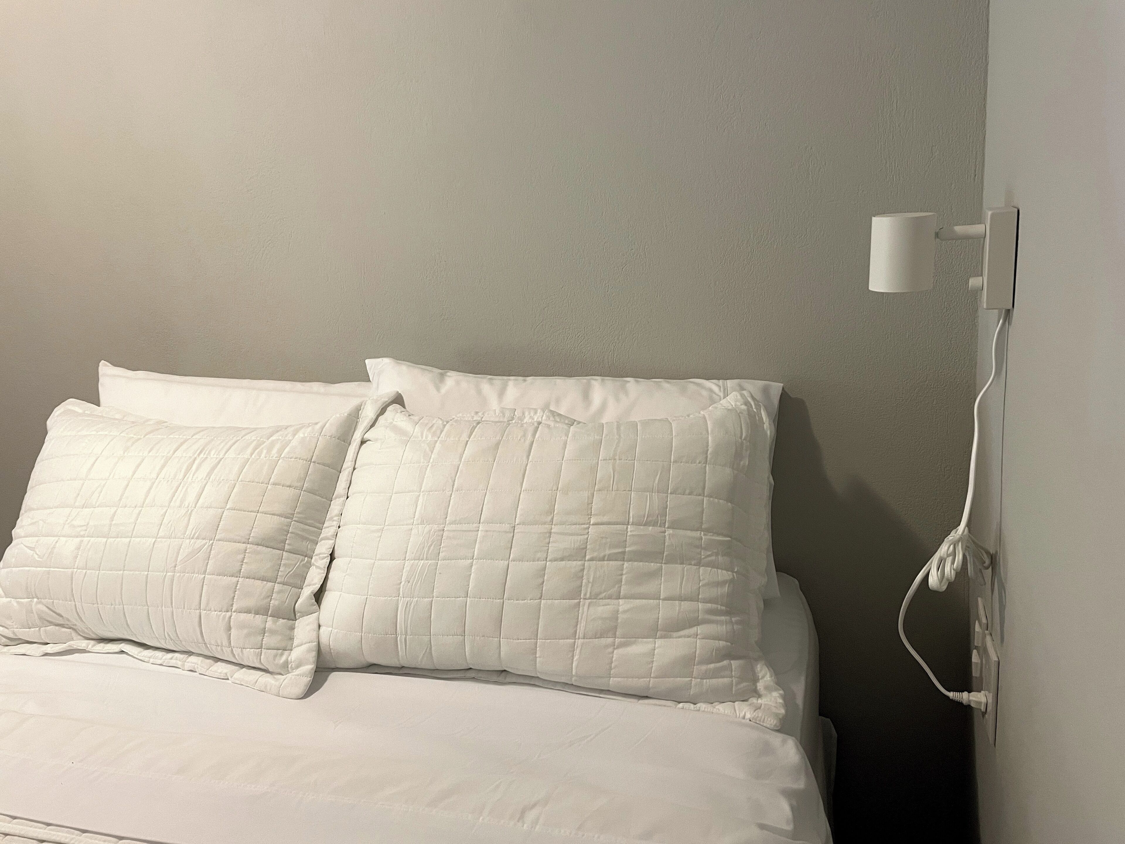 A bed with white bedding and a wall-mounted power outlet.