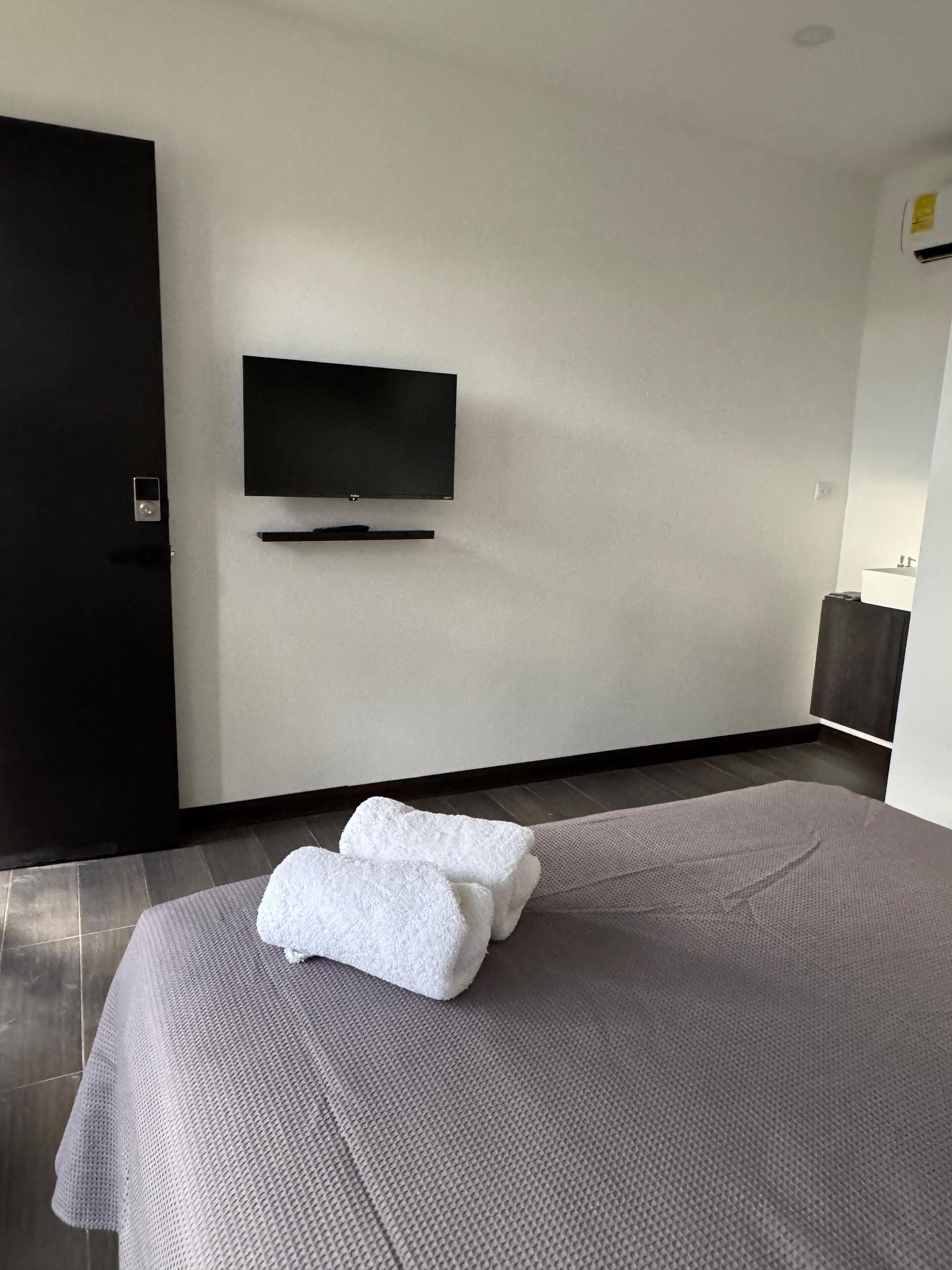 Et moderne hotelværelse med en stor seng, et fladskærms-tv ophængt på væggen og en mørk dør.