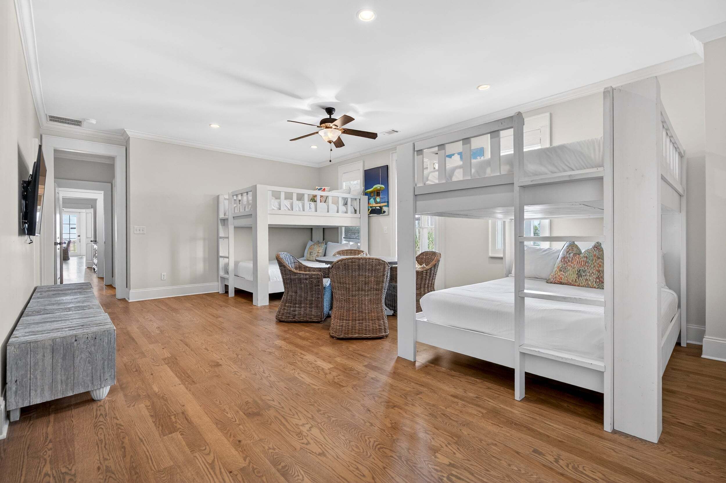 A room with bunk beds, a ceiling fan, a dining table with chairs, and a bench.
