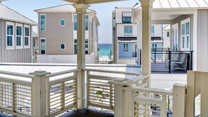 A coastal building with a balcony overlooking the sea, featuring a white railing and a covered porch area.